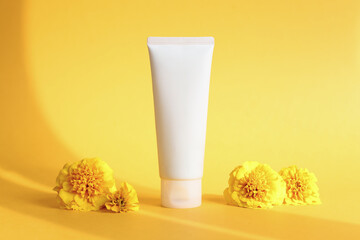 White squeeze bottle cosmetic cream tube and marigolds flowers on yellow background with shadow....