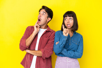 Young mixed race couple isolated on yellow background thinking an idea pointing the finger up