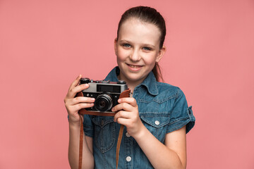 Happy girl posing with vintage photo camera and feeing satisfied. Indoor studio shot isolated on pink background