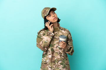 Military mixed race woman isolated on blue background holding coffee to take away and a mobile