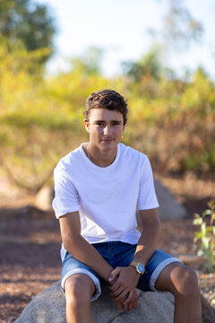 teen boy wearing white tee shirt sitting on rock