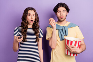 Photo of shocked excited couple wear casual clothes 3d spectacles holding tv remote eating pop corn isolated violet color background