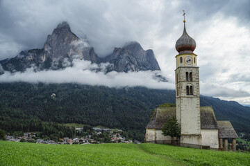 Fototapeta na wymiar St Valentine's Church, Seis am Schlern, Italy. Schlern mountain with rainy clouds in background
