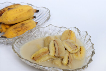 Naklejka na ściany i meble Homemade cultivated banana in coconut milk recipe on white background. One of popular traditional dessert of Thailand and Southeast Asia.