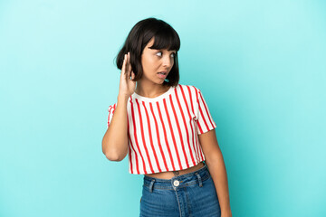 Young mixed race woman isolated on blue background listening to something by putting hand on the ear