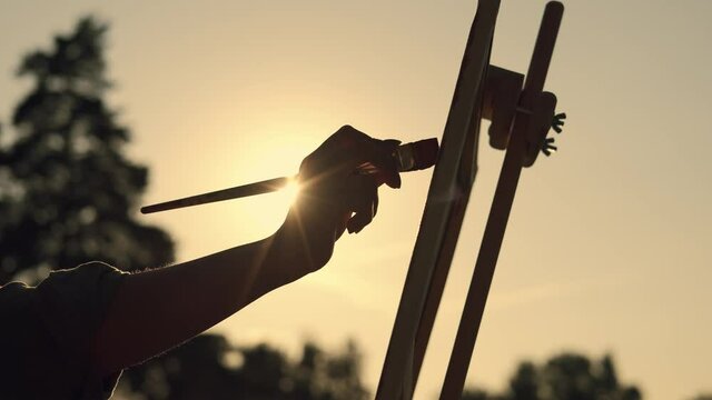 The artist's hand paints a picture during sunset. Woman Artist, Art for Sales, Inspiration in Nature.