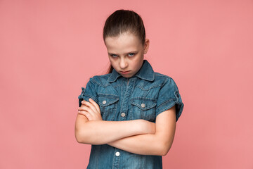 Portrait of funny frustrated naughty little girl looking at camera with comical resentful unhappy face expression. Indoor studio shot isolated on pink background