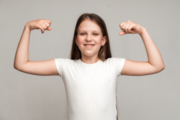Look at my muscle, I'm strong. Portrait of adorable little girl in T-shirt showing her biceps and strength, feeling powerful and self-confident. Indoor studio shot