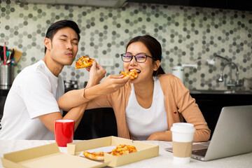 Asian couple eating pizza together in the kitchen.