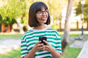 Young brunette woman in the park using mobile phone and looking up