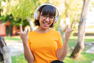 Young brunette woman in the park listening music making rock gesture