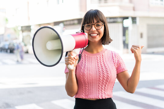 Young brunette woman in the city shouting through a megaphone and pointing side
