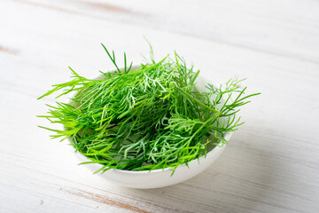 Fresh dill on a plate on a white wooden background. Cooking ingredient.