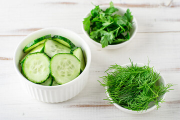 Fresh chopped cucumber, parsley, dill on a white wooden background. Salad ingredients. Vegan food concept.