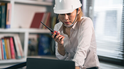 A female engineer is using a radio to contact work. at the desk  - obrazy, fototapety, plakaty