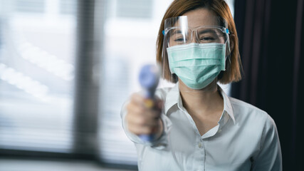 Close-up shot of doctor wearing protective mask ready to use infrared forehead thermometer (thermometer gun) to check body temperature for virus symptoms - epidemic virus outbreak concept