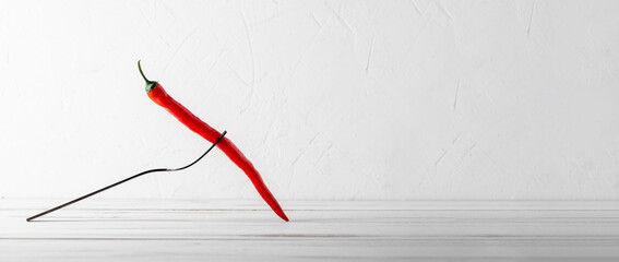 Red hot chili peppers on a fork on a white wooden background. Spicy food concept.