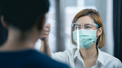 Close-up shot of doctor wearing protective mask ready to use infrared forehead thermometer (thermometer gun) to check body temperature for virus symptoms - epidemic virus outbreak concept