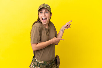 Military caucasian woman with dog tag isolated on yellow background surprised and pointing side