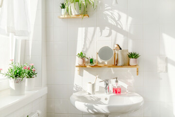 White bathroom in eco friendly style with a sink next to a window at sunny day. Green plans on wooden bamboo shelves and shadows on the background. Zero waste and sustainable life style. Wellness
