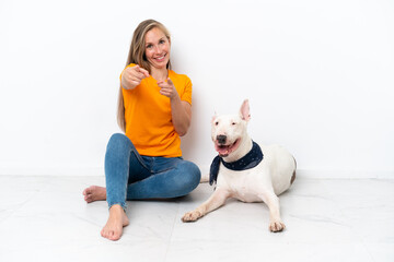 Young English woman sitting on the floor with her dog isolated on white background points finger at you with a confident expression