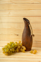 GGrape jug on a wooden natural background. Rustic retro style. Antique clay jug with wine. Green juicy ripe grapes of the autumn harvest. the concept of agriculture, winemaking. Horizontal still life