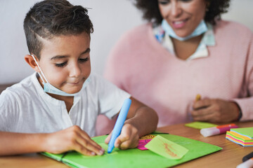 Naklejka premium Teacher doing painting activities with boy while wearing safety face mask under chin - Concept of preschool and daycare