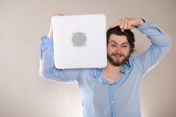 Young attractive man  holding white portable bluetooth speaker on shoulder on gray background