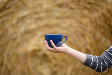 Female hand holds a porcelain cup of coffee on a natural background. Selective focus on the cup.