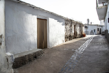 Fototapeta na wymiar Laroles street with whitewashed walls with a door and bench attached to the facade and a typical Alpujarra fireplace in the background