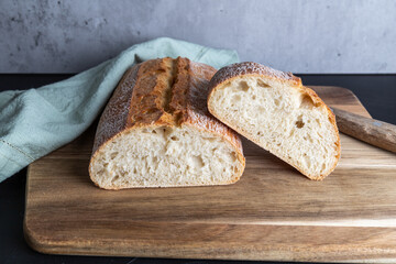 Fresh ciabatta cut in half, covered with a kitchen towel, lies on the wooden board, copy space