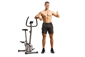 Shitless fit man leaning on an exercise bike and gesturing a thumb up sign
