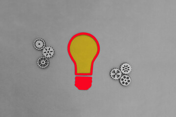 A red light bulb, wooden gears on a gray background. Joint business ideas, creativity.
