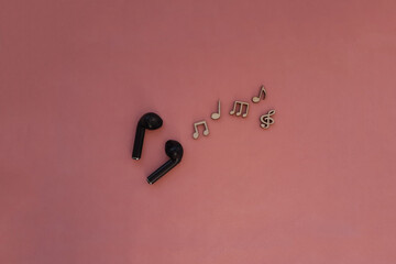 Wireless headphones are black, wooden notes on a pink background. Listening to songs, melodies, music.