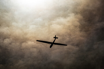 A glider is towed up to altitude under a overcast layer of clouds.