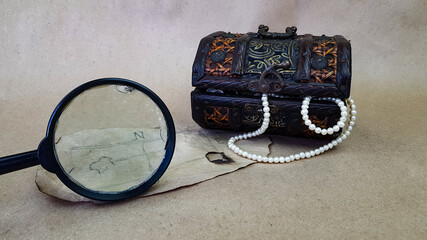 a treasure chest and an old map on a light next to a magnifying glass. there are pearls and shells...