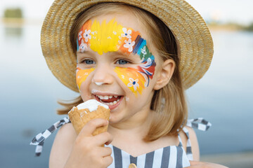 Happy child with face art paint eating ice-cream at summertime