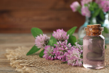 Beautiful clover flowers and bottle of essential oil on wooden table, closeup. Space for text