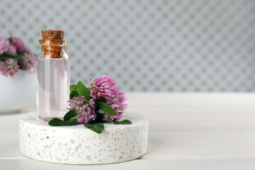 Obraz na płótnie Canvas Beautiful clover flowers and bottle of essential oil on white wooden table. Space for text