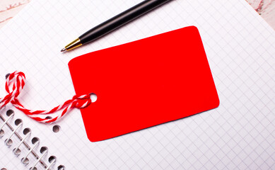 There is a pen and a red-colored price tag on a string with a place to insert text on a white...