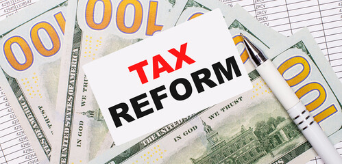 Against the background of reports and dollars - a white pen and a card with the text TAX REFORM. Business concept