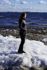 A young slender girl stands on the ice by the sea. Winter landscape