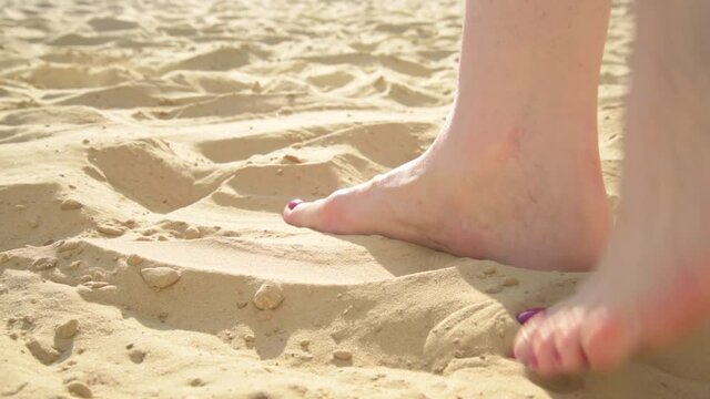 Female feet with painted nails close-up. The feet are massaged in the sand. Feet shift from foot to foot in the sand on the beach. Useful walking barefoot on the sand. Prevention of flat feet