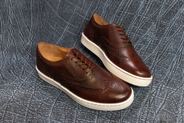 Formal golf wingtip sneakers on a blue textured leather background. The mens fashion footwear has a white outsole and is a fancy sneaker.