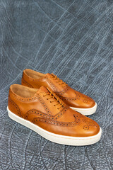 Formal golf wingtip sneakers on a blue textured leather background. The mens fashion footwear has a white outsole and is a fancy sneaker.