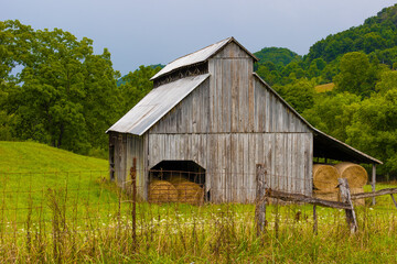 Barn full of rolled gray hay sits on hillside pasture in rural Virginia