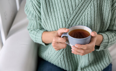 Woman with cup of hot tea indoors, closeup. Cozy home atmosphere