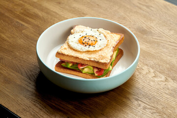 French sandwich Croque Madame with egg, cucumber, tomatoes, avocado and herring caviar in a plate on a wooden background