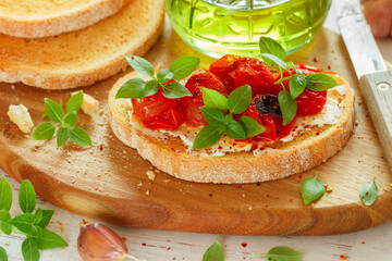 Bruschetta with baked cherry tomatoes, cream cheese (cottage cheese or ricotta), garlic, fresh basil and spices close-up. Mediterranean cuisine. A gourmet snack. Selective focus