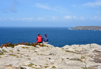 Fototapeta na wymiar Two unidentified people sitting on the rocks by the sea and enjoying the view over the coast of brittany, France